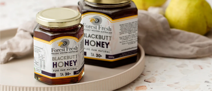 Two jars of Forest Fresh Blackbutt honey, TA35+ and TA30+, on a ceramic plate with linen and fruit